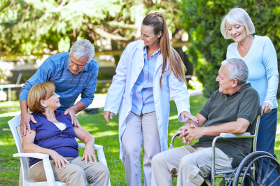 Many seniors relaxing in a park of a nursing home with geriatric nurse